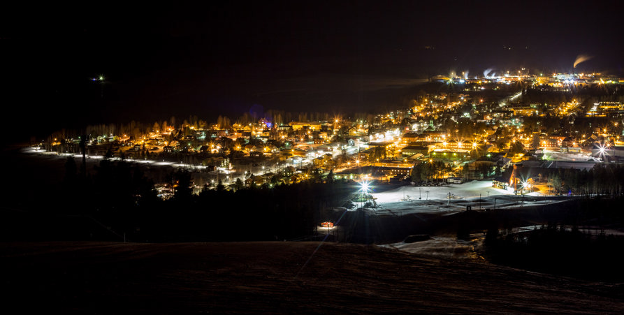 Vy över Malå samhälle fotad från berg en mörk natt. Lampor lyser upp gatorna.