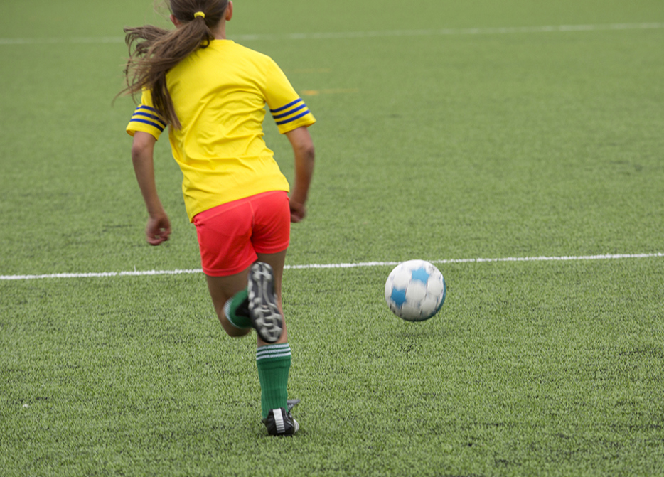 Ung tjej som springer med boll på fotbollsplanen. 